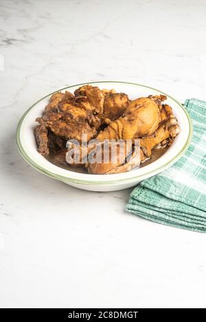 A serving of Filipino-style chicken adobo dish in a bowl with a green napkin set on a marble tabletop. Stock Photo