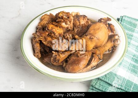 A serving of Filipino-style chicken adobo dish in a bowl with a green napkin set on a marble tabletop. Stock Photo