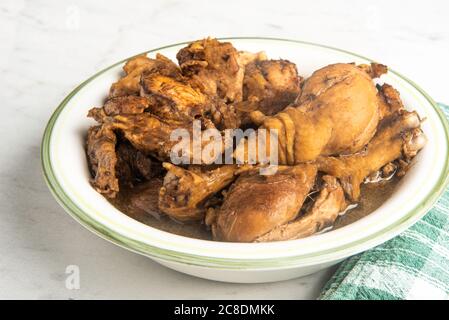 A serving of Filipino-style chicken adobo dish in a bowl with a green napkin set on a marble tabletop. Stock Photo