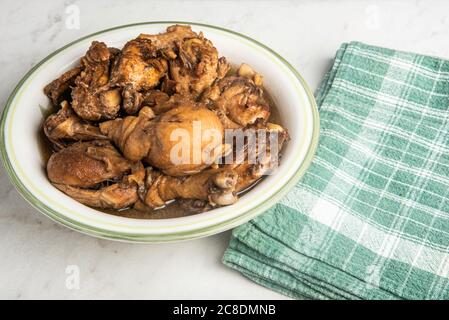 A serving of Filipino-style chicken adobo dish in a bowl with green napkin set on a marble tabletop. Stock Photo