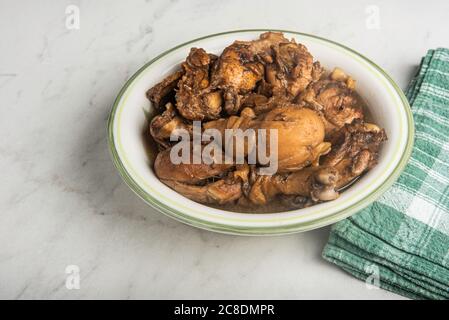 A serving of Filipino-style chicken adobo dish in a bowl with green napkin set on a marble tabletop. Stock Photo