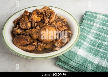 A serving of Filipino-style chicken adobo dish in a bowl with green napkin set on a marble tabletop. Stock Photo