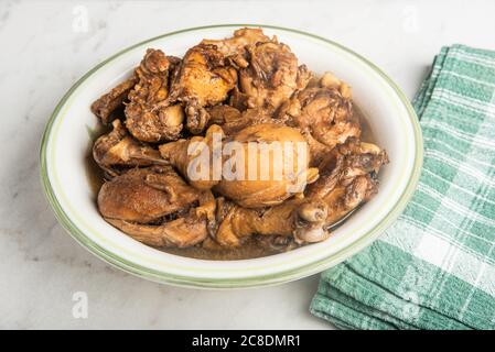 A serving of Filipino-style chicken adobo dish in a bowl with green napkin set on a marble tabletop. Stock Photo