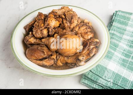 A serving of Filipino-style chicken adobo dish in a bowl with green napkin set on a marble tabletop. Stock Photo