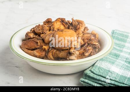 A serving of Filipino-style chicken adobo dish in a bowl with green napkin set on a marble tabletop. Stock Photo