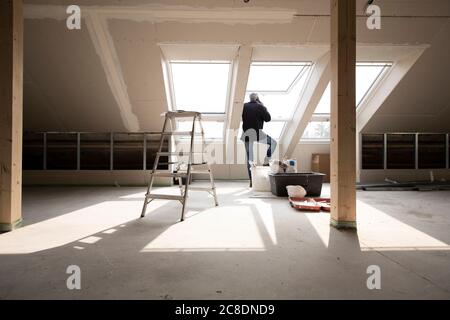 Male architect talking over smart phone while standing by window at home under construction Stock Photo
