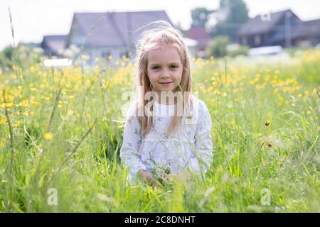 Smiling girl holding flowers sitting on grassy land Stock Photo
