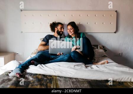 Couple watching movie sitting on bed at home Stock Photo