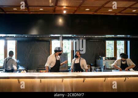 Chefs wearing protective face masks working together in restaurant kitchen Stock Photo
