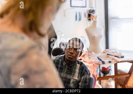 Young male trainee looking at senior designer teaching in fashion studio Stock Photo