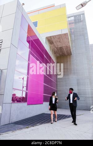 Business professionals wearing masks talking while walking on footpath in city Stock Photo