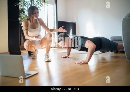Woman motivating man in doing push-ups on hardwood floor at home Stock Photo