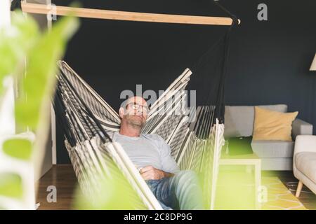 Mature man sleeping on hammock in living room at home Stock Photo