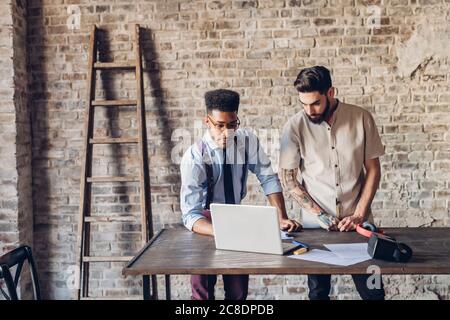 Two creative businessmen using laptop in loft office Stock Photo