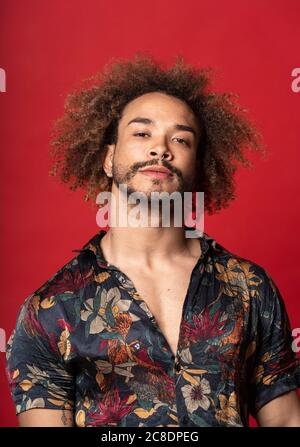 Handsome young man with curly hair standing against red background Stock Photo