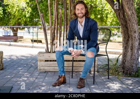 Smiling handsome young male professional sitting with hands clasped at cafe Stock Photo