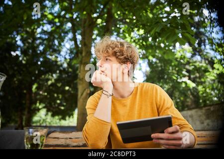 Portrait of pensive young man with digital tablet outdoors Stock Photo