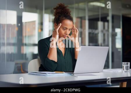 Portrait of pensive businesswoman at desk looking at laptop Stock Photo