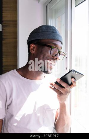 Happy young man using smart phone by window Stock Photo