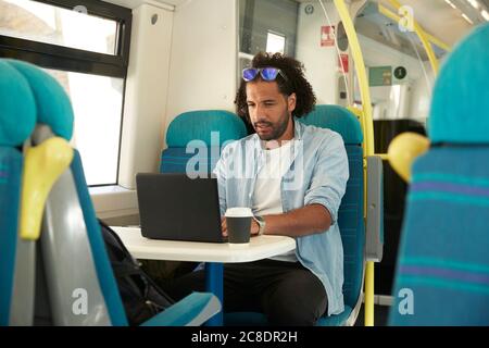 Young trendy man using laptop in train Stock Photo