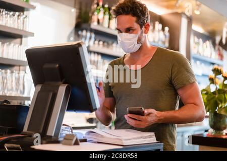Restaurant manager with protective mask using computer and smartphone Stock Photo