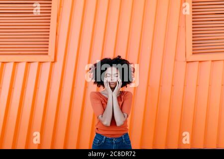Young afro woman with eyes closed standing against orange metal wall Stock Photo