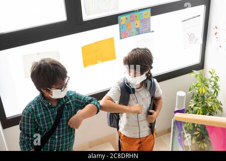 Schoolboys wearing masks giving elbow bump while standing on steps Stock Photo