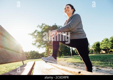 Female jogger stretching her leg on bench in park Stock Photo