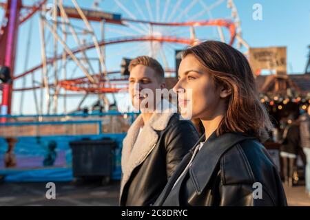 Young couple looking away while standing at amusement park during sunset Stock Photo