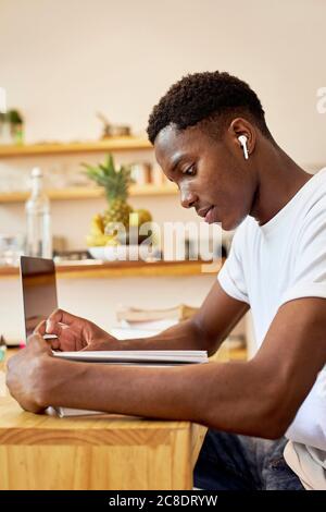 Close-up of young man listening music while studying on table at home Stock Photo