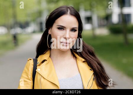 Beautiful young woman with long brown hair wearing yellow leather jacket in city Stock Photo