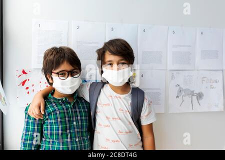 Friends wearing masks standing against wall in school Stock Photo