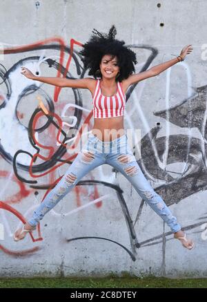 Young woman jumping in front of wall with graffiti Stock Photo
