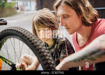Father and son repairing bicycle at yard during sunny day Stock Photo