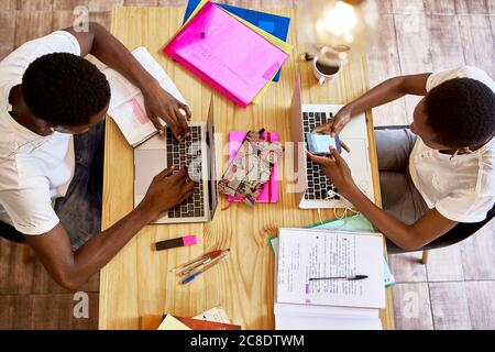 Young woman using smart phone while boyfriend studying over laptop on table at home Stock Photo