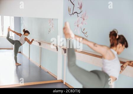 Reflection of ballerina doing stretching exercises in mirror at dance studio Stock Photo