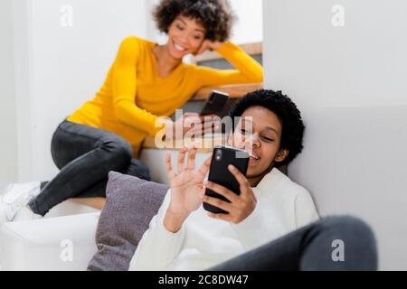 Two young women relaxing at home using their smartphones Stock Photo