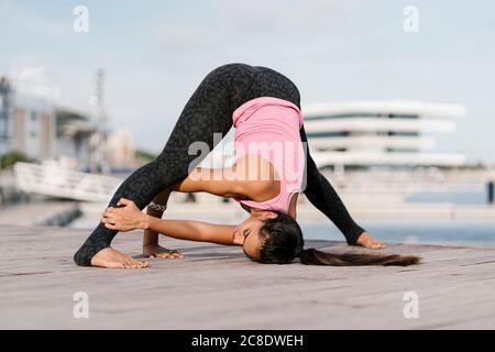 Female athlete practicing wide-legged forward bend on pier against sky Stock Photo