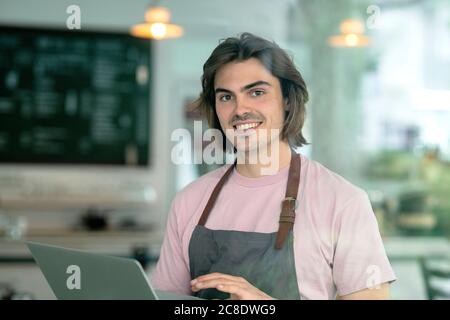 Smiling male owner using laptop while standing in coffee shop Stock Photo