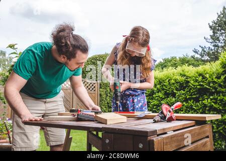 Young man looking at sister drilling on plank while standing in yard Stock Photo