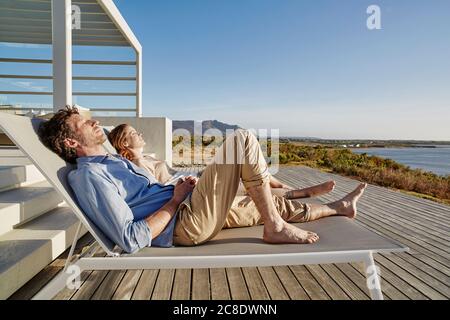 Couple lying on deck chairs at luxury beach house Stock Photo