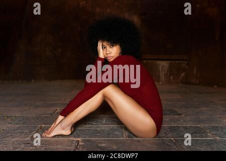 Young woman in red bodysuit sitting on ground Stock Photo