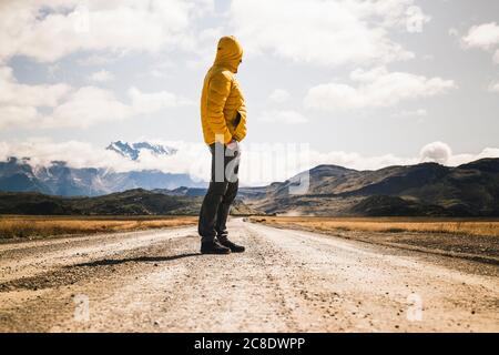 Mature man standing on dirt road against cloudy sky, Torres Del Paine National Park, Patagonia, Chile Stock Photo