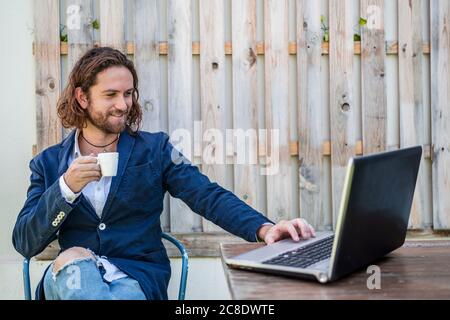 Handsome young businessman drinking espresso while using laptop at cafe Stock Photo