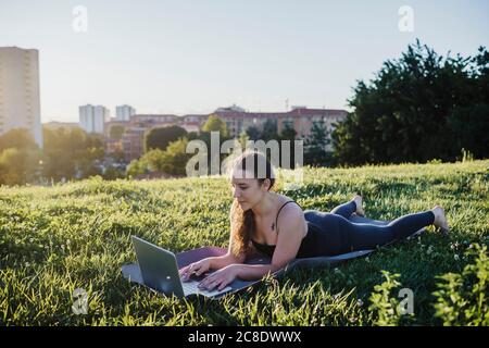 Sporty young woman using laptop while lying on exercise mat at city park Stock Photo