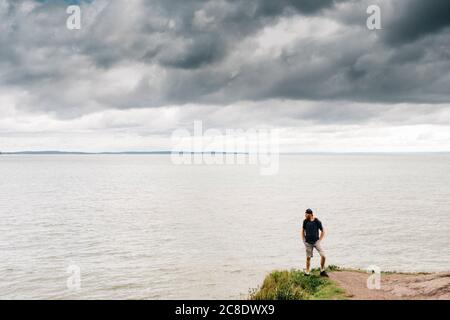 Man standing on cliff while looking at sea against storm clouds Stock Photo
