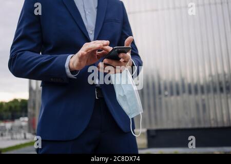 Businessman with protective face mask using smartphone in the city Stock Photo
