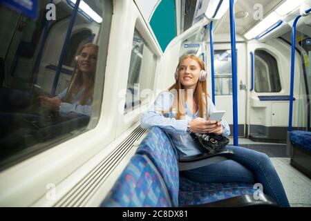 Beautiful young woman looking through window while listening music in train