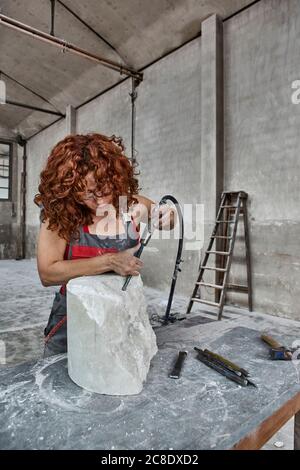 Mid adult woman carving stone with jackhammer on table in workshop Stock Photo