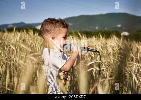 Cute boy singing over microphone while standing amidst crops during sunny day Stock Photo